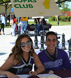 Two smiling students posing in front of a club sign