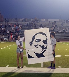 Two students holding up a large painting on the field during a game